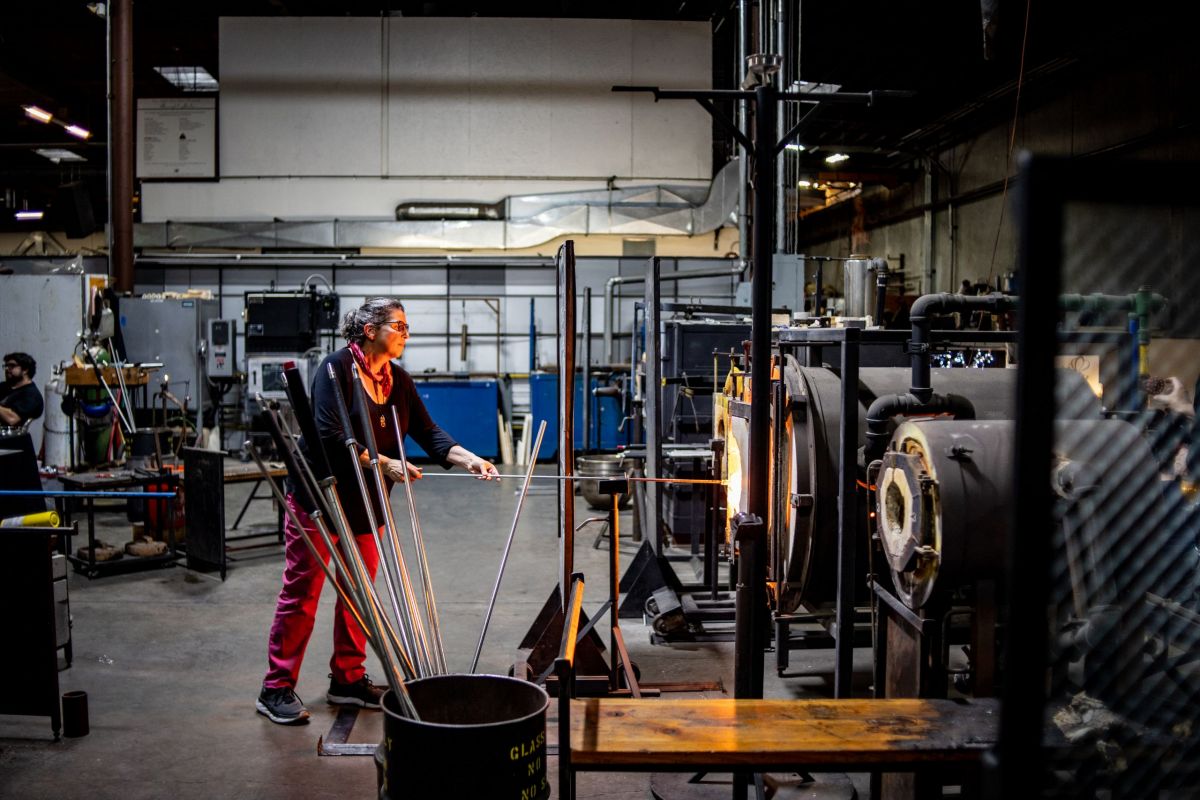 A woman stands at a glass blowing kiln