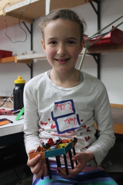 Sophie, age 8, holding up her gizmo in Youth Extreme Gizmos Spring Camp. This gizmo has a motor that makes it dance around the table on its stilt legs!